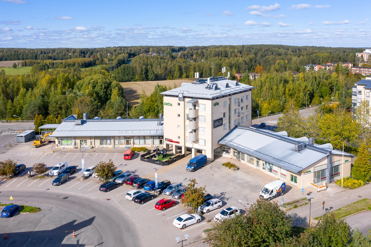 Tuusulan Hyrylänkatu 8, ilmakuva. Vaalea, monikerroksinen rakennus jonka molemmilla puolilla matalammat siivet. Talon edustalla autoja pysäköitynä pysäköintialueelle. Taustalla näkyy peltoa ja metsää.
