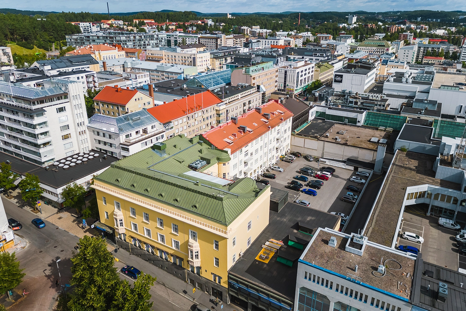 Puistonkulma-arvokiinteistö ilmakuvassa kävelykadun ja puiston kulmassa. Keltaisessa rakennuksessa on vihreä katto, sisäpihalla pysäköintitilaa.