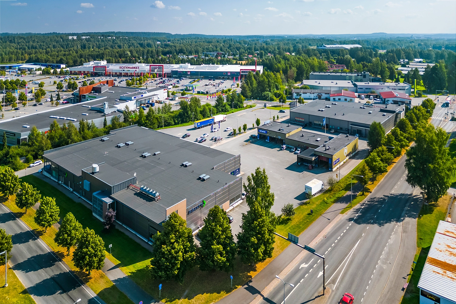 Tummanharmaa liikerakennus Tiiriön Big Box 2 ilmakuvassa. Samassa pihapiirissä on toinen liikerakennus ja katsastusasema, takana hypermarket.